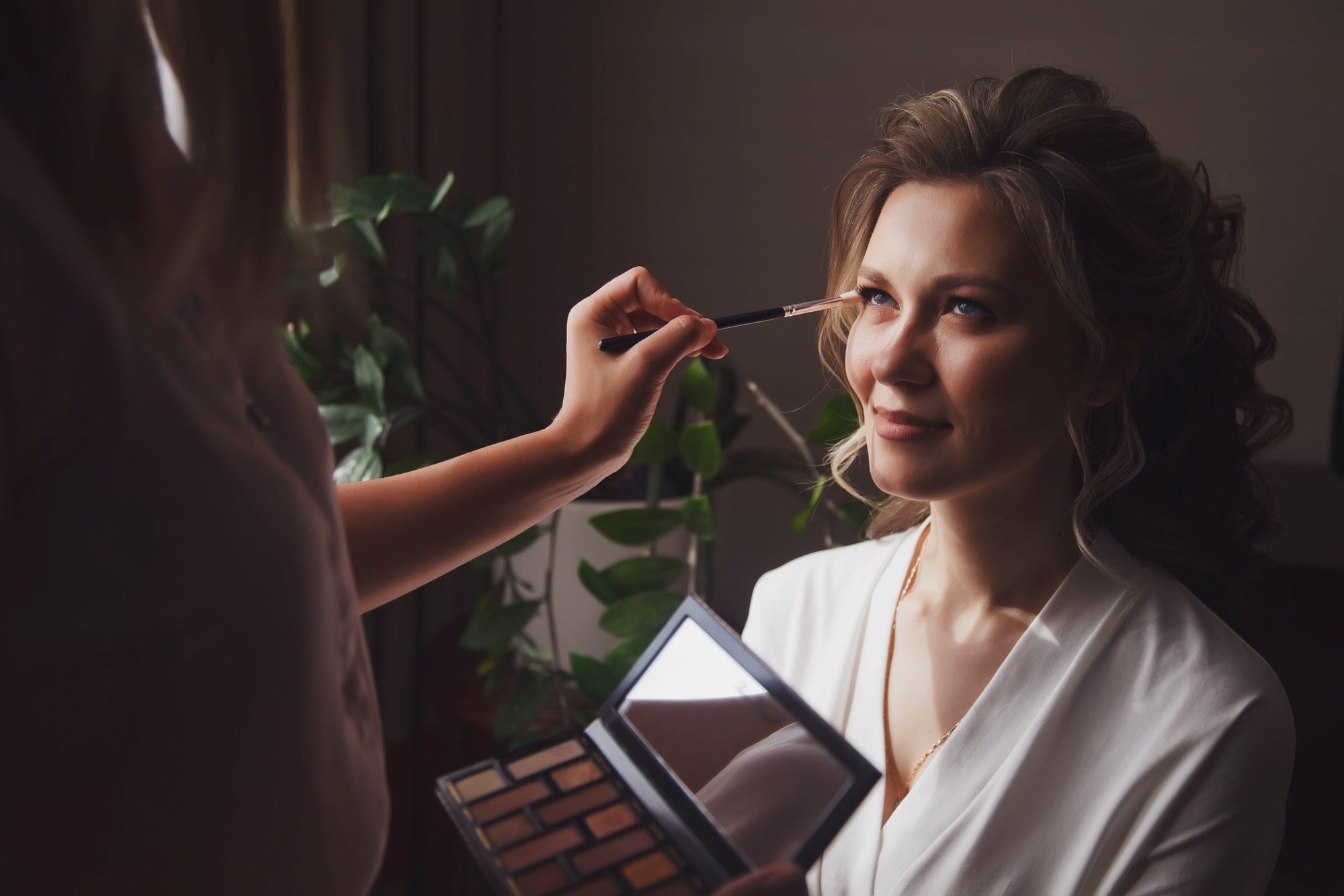 Makeup artist made wedding make-up for cute young woman bride at wedding day in hotel room